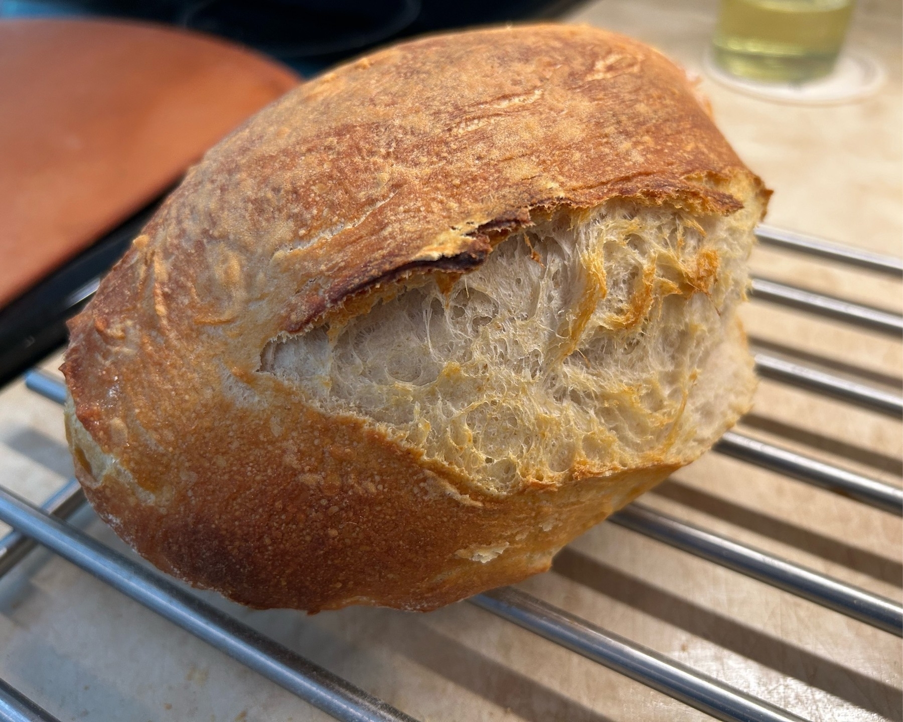 Rustic loaf of sourdough bread on a metal rack with a large diagonal opening in the bread. 