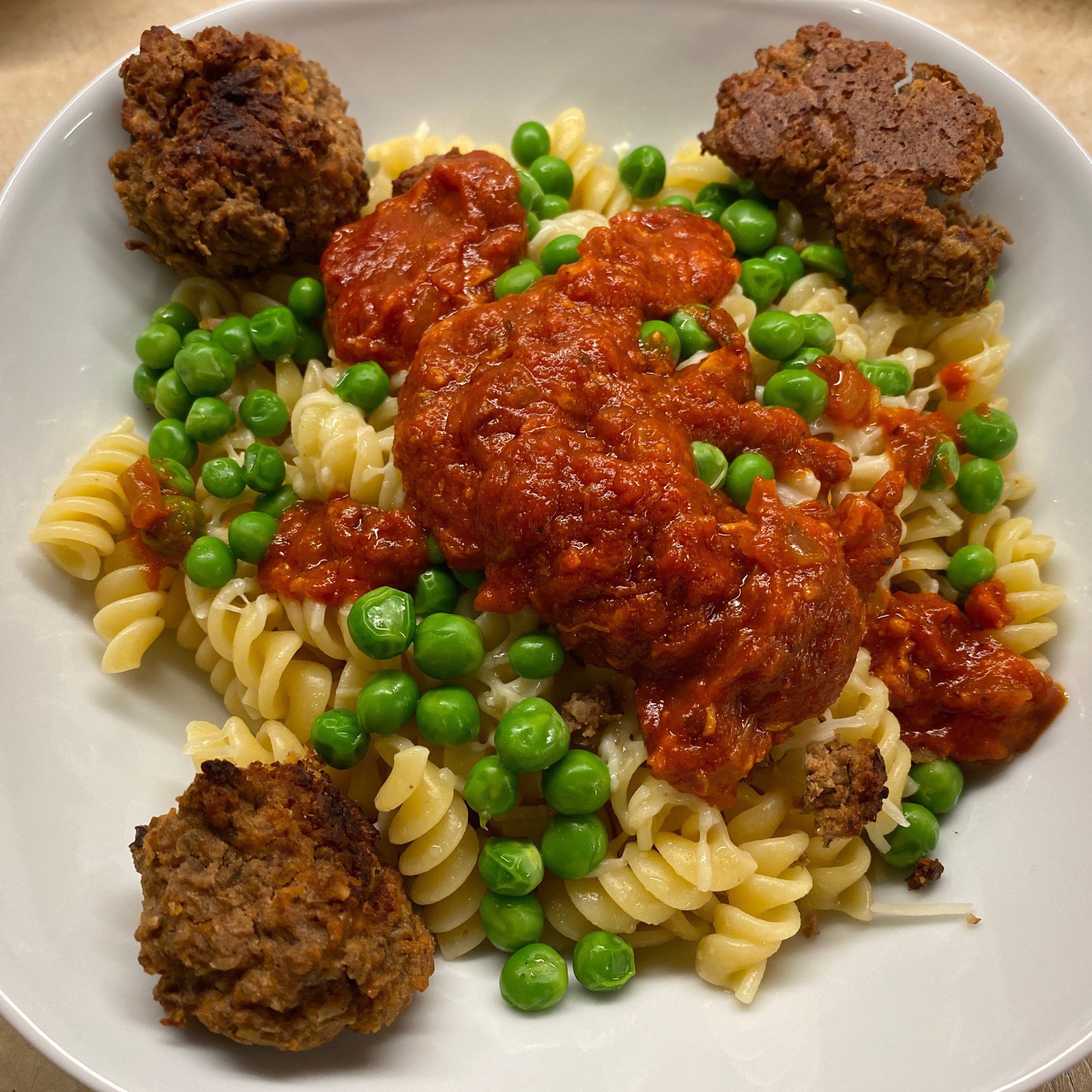 Pasta, peas, lentil balls, and sauce in a bowl.