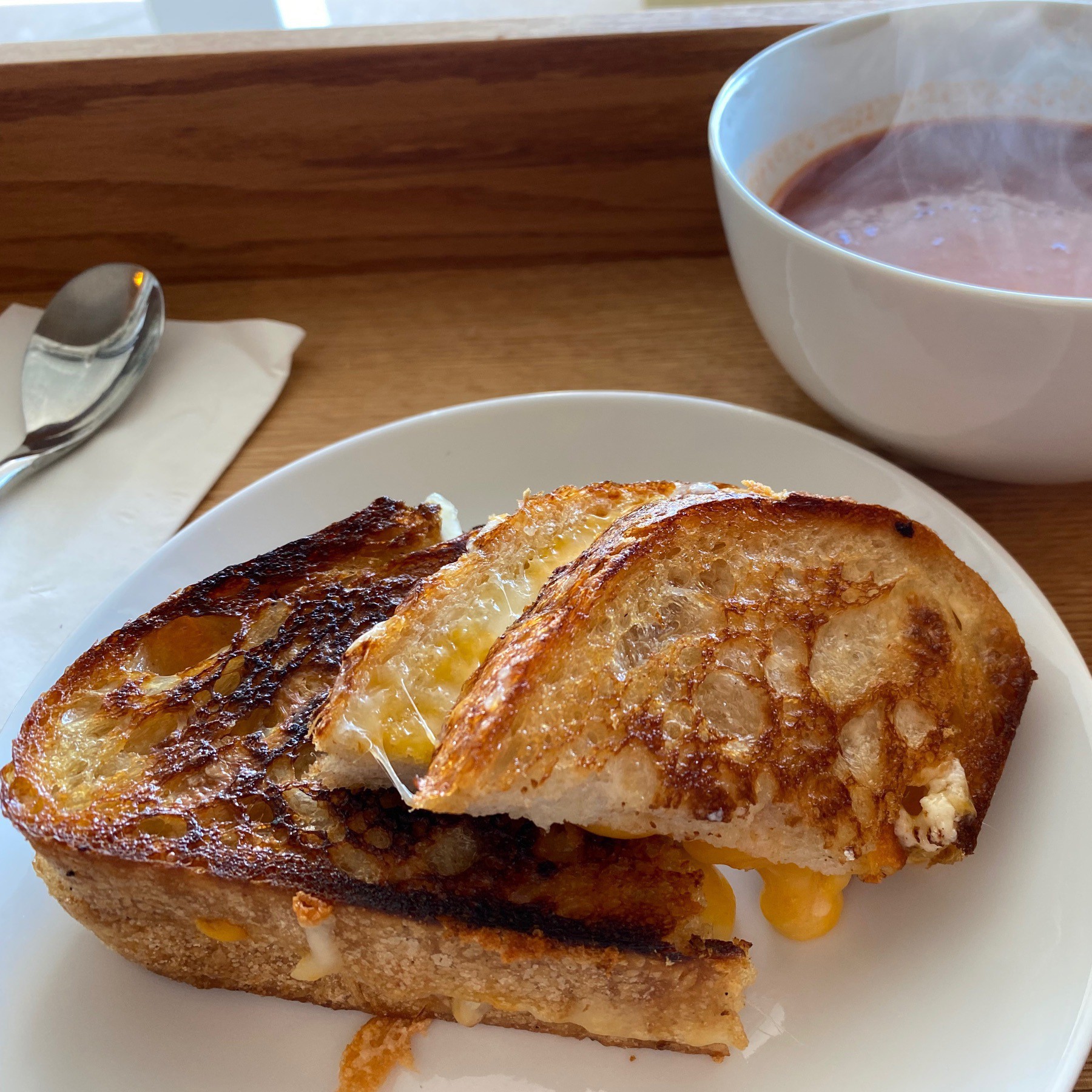Grilled cheese in plate with bowl of tomato soup in background.