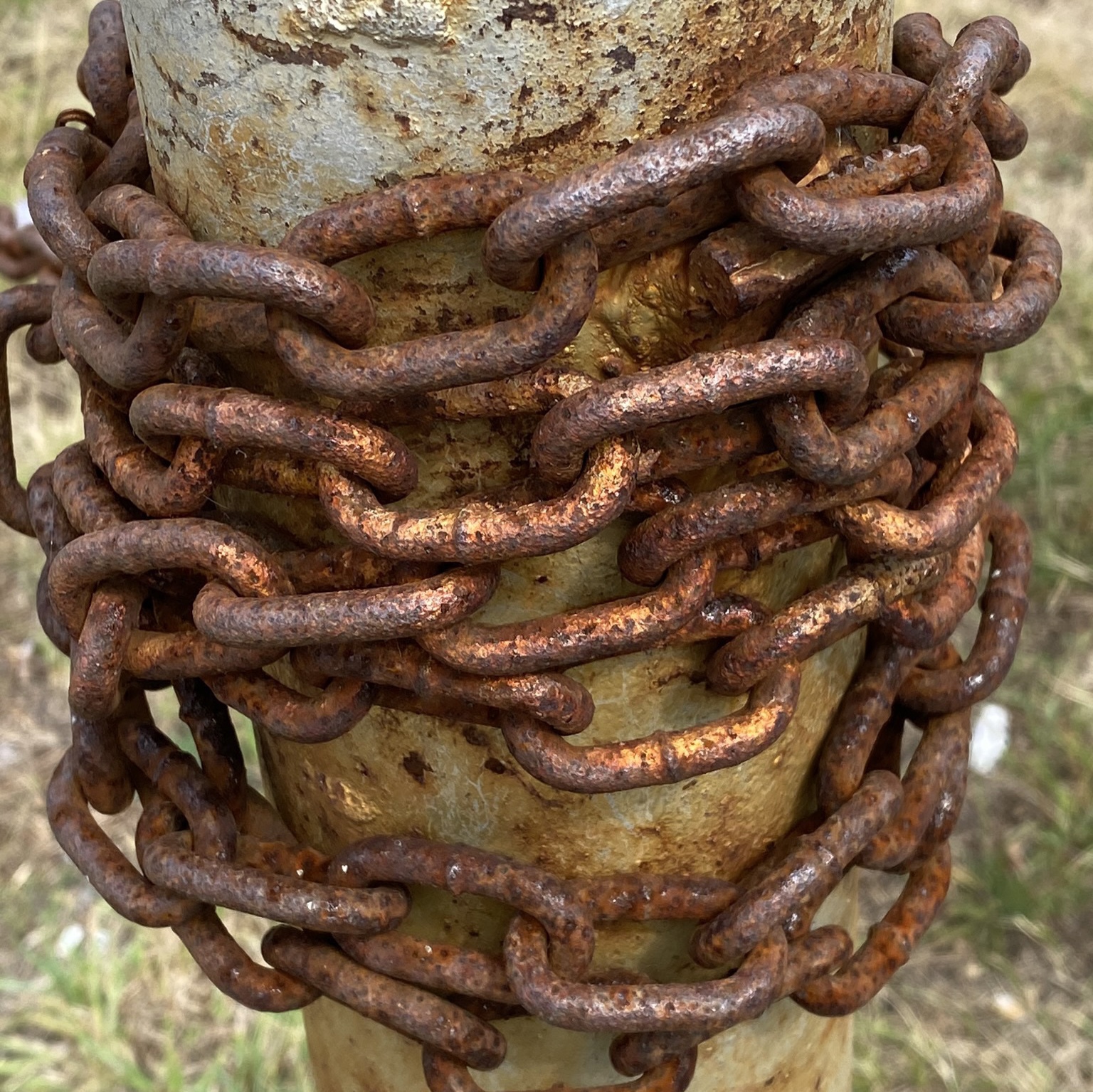 Rusting chain wrapped around metal post.