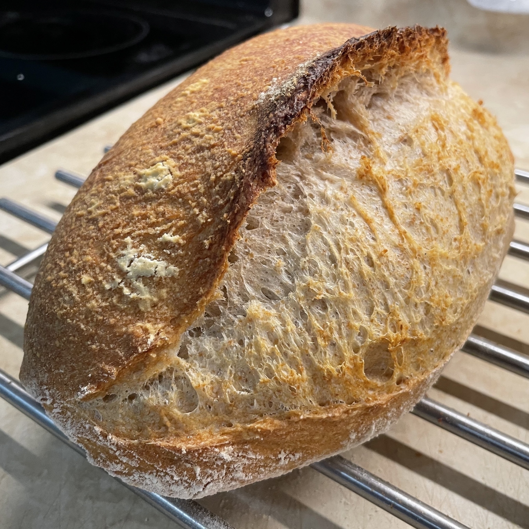 Sourdough loaf of bread cooling on metal rack.
