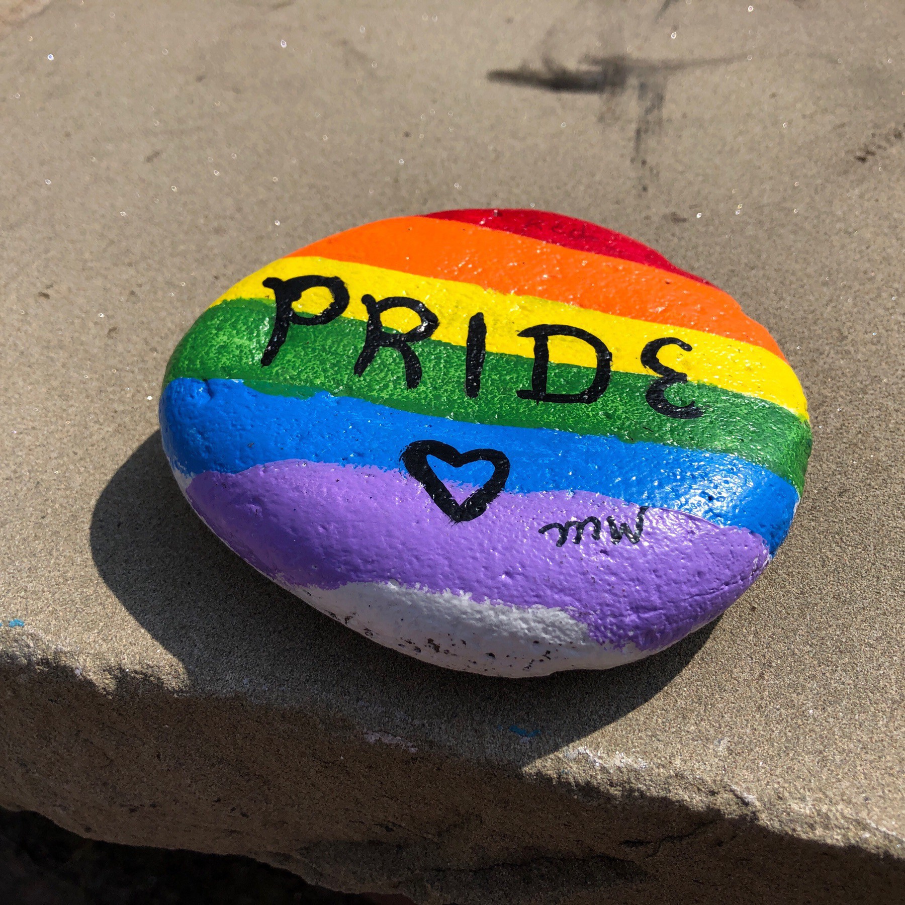 Rock painted with rainbow colours with "Pride" written on it.